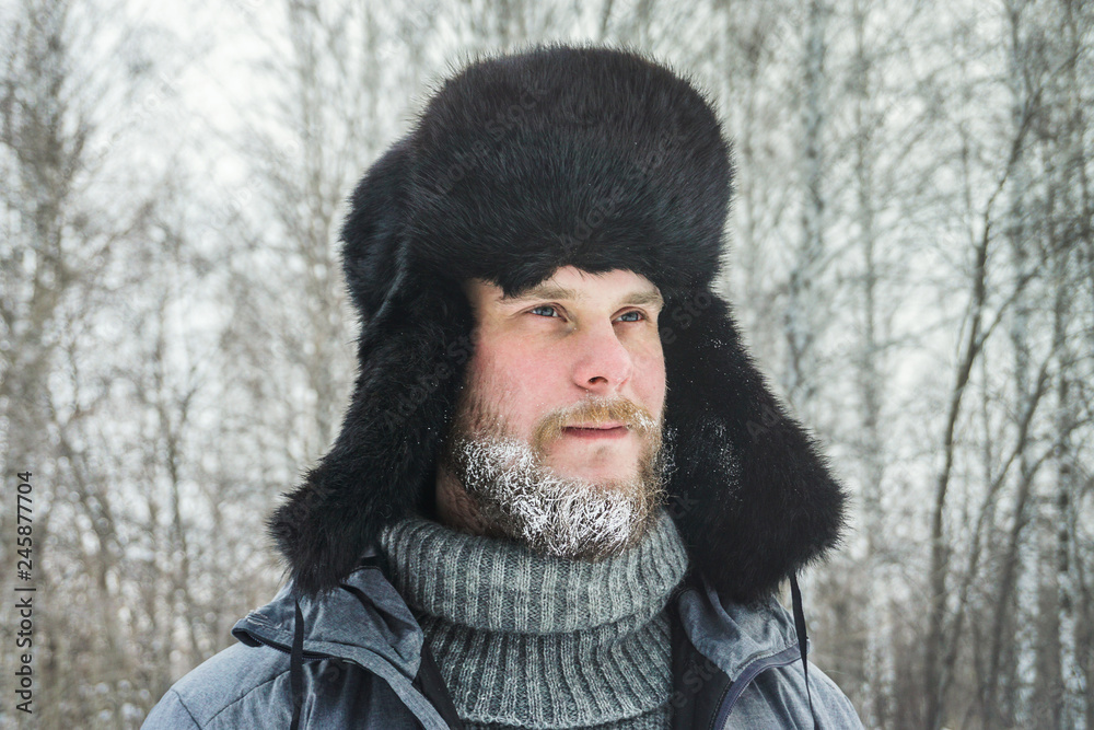 Siberian Russian man with a beard in hoarfrost in freezing cold in the winter freezes in a village in a snowdrift and wears a hat with a earflap. Siberian Russian man with a beard in hoarfrost in freezing cold in the winter freezes in a village in a snowdrift and wears a hat with a earflap.
