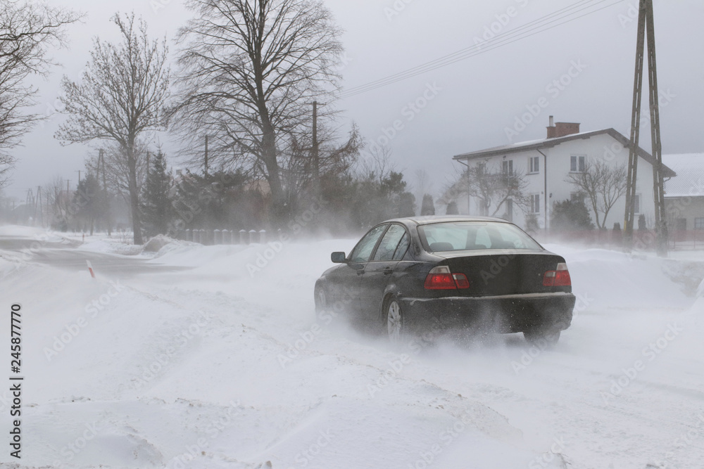 A car sneaks through drifts on a dangerous road covered with snow. Private transport is struggling with the winter elements. Difficulties in traffic during a snowstorm.The consequences of cold weather