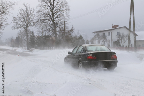 A car sneaks through drifts on a dangerous road covered with snow. Private transport is struggling with the winter elements. Difficulties in traffic during a snowstorm.The consequences of cold weather © Xato Lux