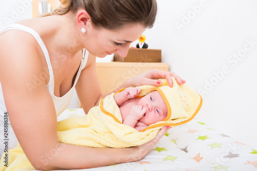 Close-up of smiling mother covering her baby in yellow towel after having bath