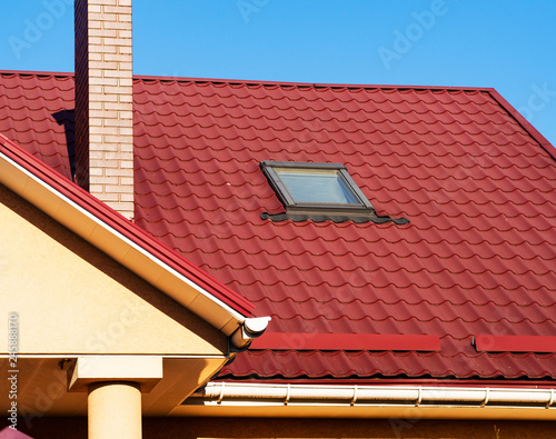 Skylight, snowguard and brick chimney on metal tile roof, close up photo