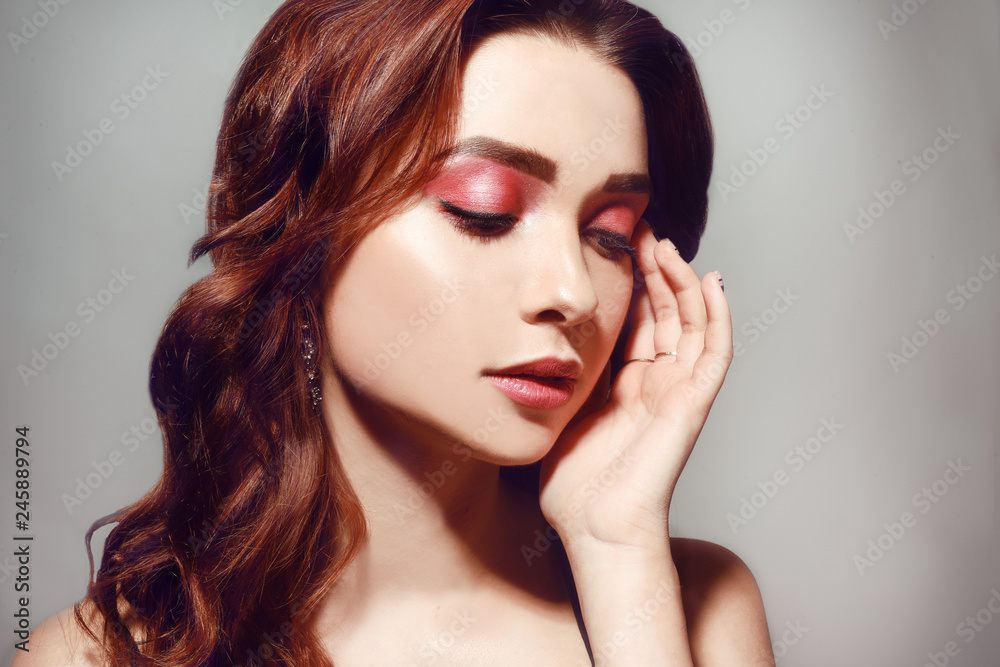 Fototapeta premium Beautiful caucasian woman with short brown curly hair. Portrait of a pretty young adult girl. Sexy face of an attractive lady posing at studio over grey background. Woman with pink natural make up.