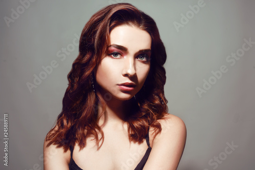 Beautiful caucasian woman with short brown curly hair. Portrait of a pretty young adult girl. Sexy face of an attractive lady posing at studio over grey background. Woman with pink natural make up.