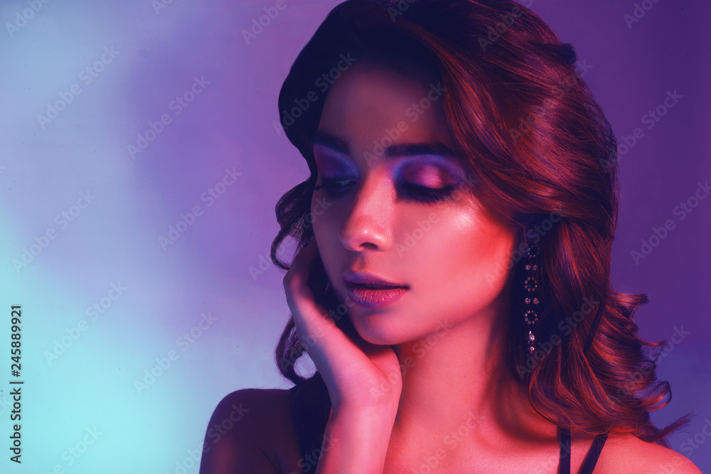 Fashion portrait of young elegant girl in jewelry. Colored background, studio shot. Beautiful brunette woman. Girl posing in neon light. Woman with stylish hair and pink lips and cerly hair. Beauty.