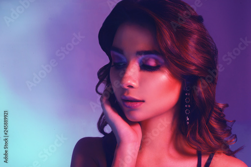 Fashion portrait of young elegant girl in jewelry. Colored background, studio shot. Beautiful brunette woman. Girl posing in neon light. Woman with stylish hair and pink lips and cerly hair. Beauty.