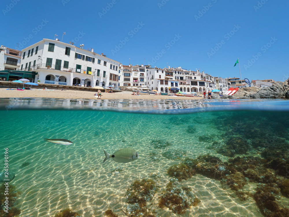 Spain Calella de Palafrugell Mediterranean village, beach shore with fish underwater sea, Costa Brava, Catalonia, split view half over and under water