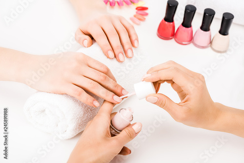 Girl holding hands on towel while manicurist applying nail polish
