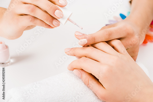 Partial view of manicurist gently holding hand while applying nail polish