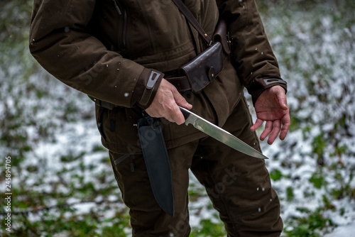 the hunter pulls out a knife in the winter forest