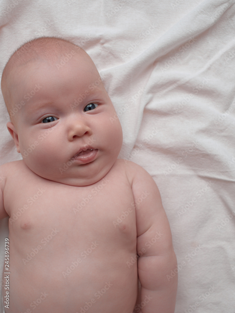 Baby with a calm expression. The baby lies on a white linen cloth. Baby with a calm expression. The baby lies on a white linen cloth.