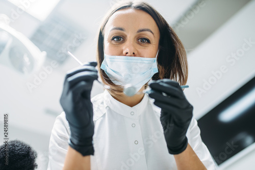 Dentist in mask and gloves holds instrument