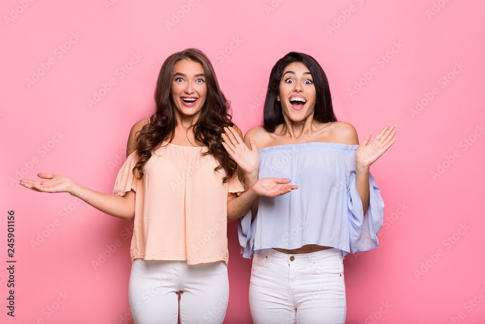 Excited female friends standing over pink background Excited female friends standing over pink background