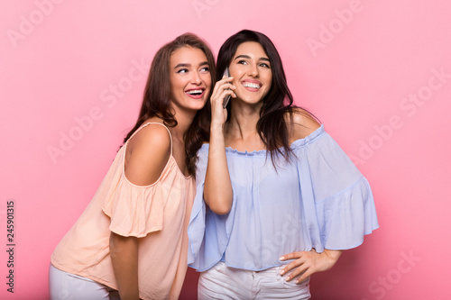 Happy women enjoying phone talk on pink background