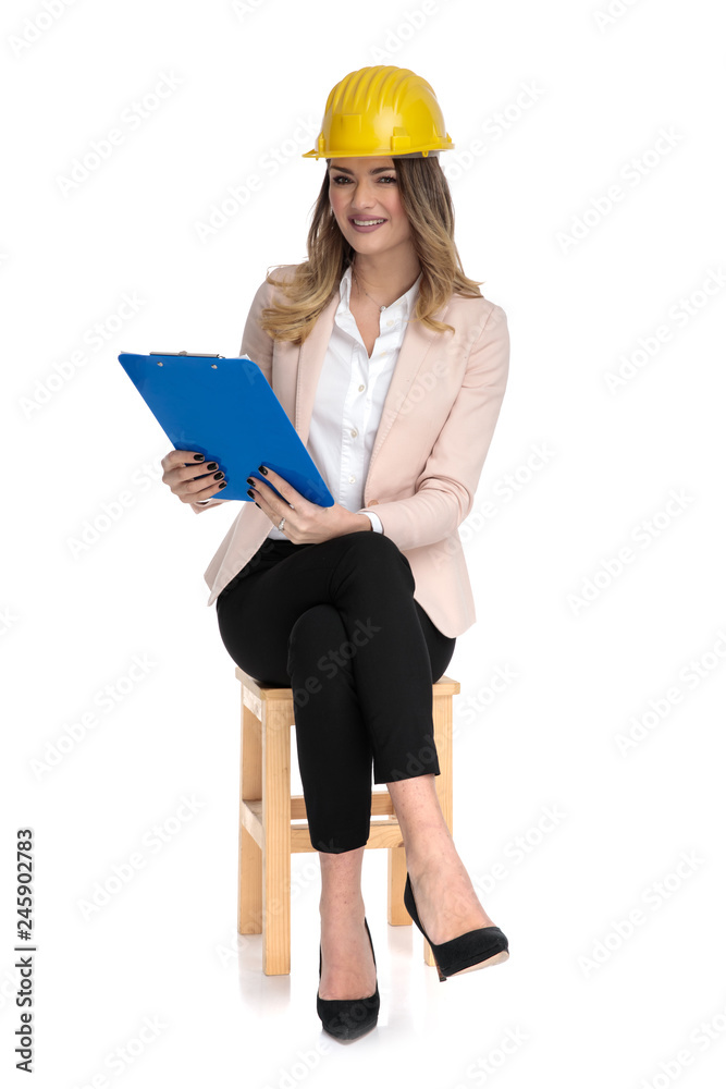young businesswoman wearing engineer hat holds blue clipboard young businesswoman wearing engineer hat holds blue clipboard