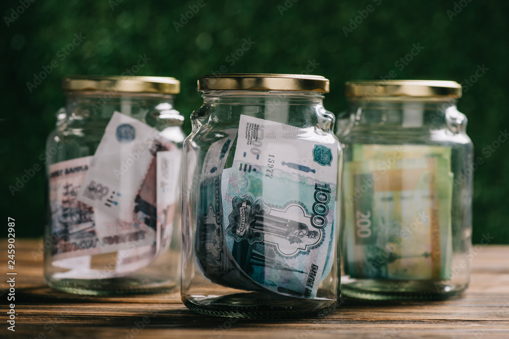 close-up view of glass jars with russian rubles banknotes on wooden table close-up view of glass jars with russian rubles banknotes on wooden table