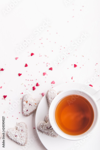  White tea cup with tea and Valentine's day white coconut heart shaped cookies with red and pink heart sprinkles. Copy space
