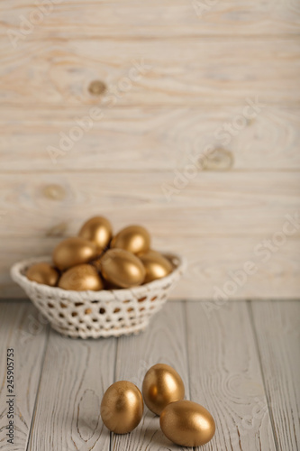 Happy easter! Easter eggs of golden color on a light wooden background.
