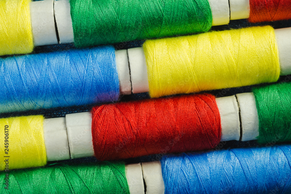 Spools of blue, yellow, red and green sewing thread arranged in rows on denim Spools of blue, yellow, red and green sewing thread arranged in rows on denim