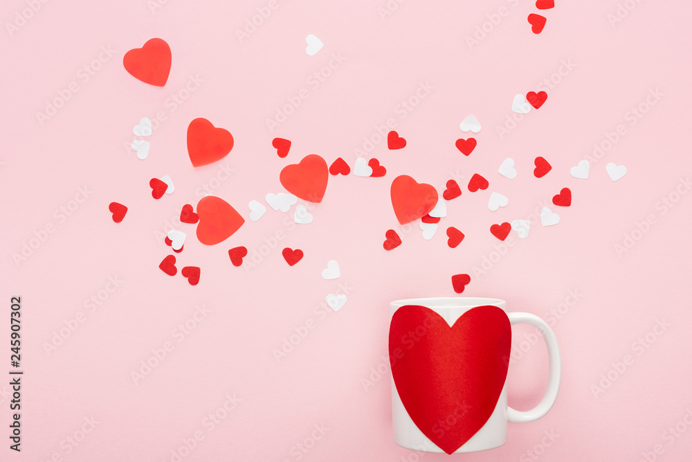 top view of paper hearts and cup with heart shaped sticker isolated on pink, st valentines day concept