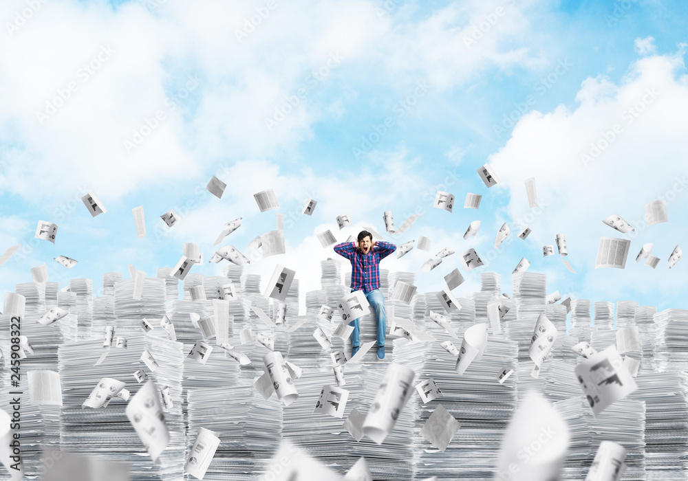 Attractive man sitting on pile of paper documents.