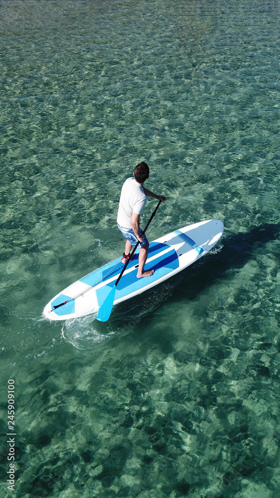 Aerial drone bird's eye view photo of man exercising Stand Up Paddle surf board or SUP in tropical exotic bay with emerald clear sea