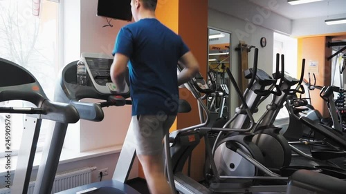 Legs of unrecognizable man running on the treadmill in the fitness studio. Left side low angle medium shot