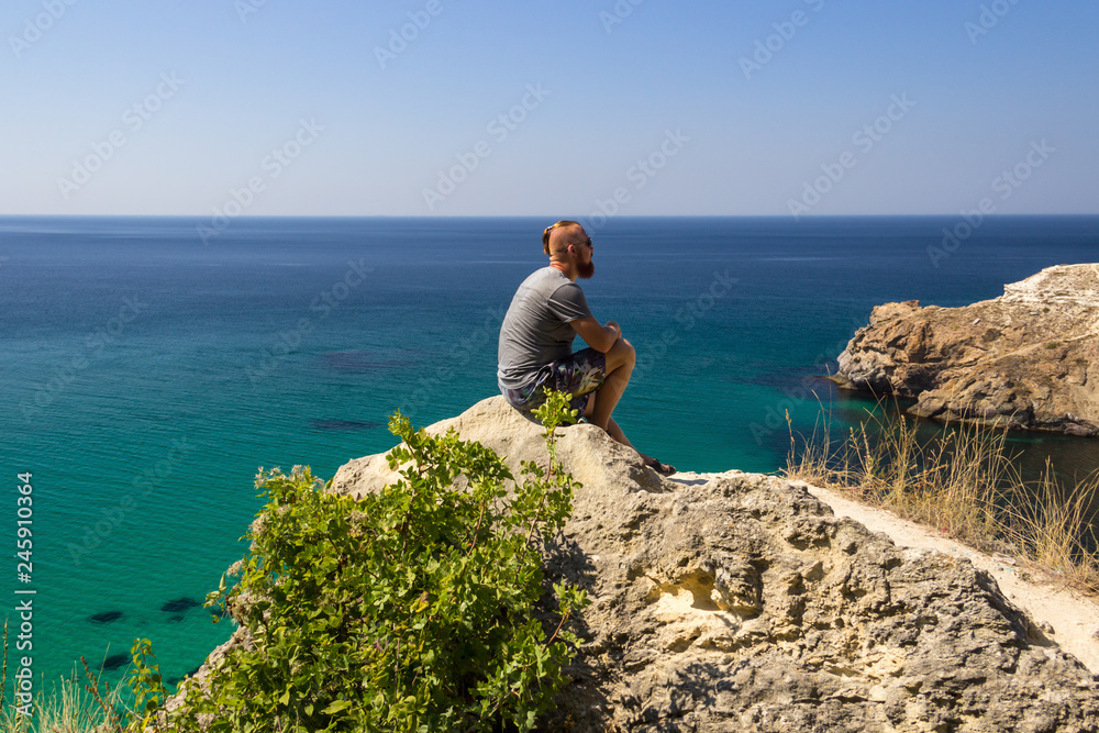 A man in a gray T-shirt sits by the turquoise sea. Beautiful view of the sea.