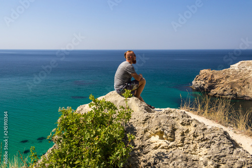A man in a gray T-shirt sits by the turquoise sea. Beautiful view of the sea.