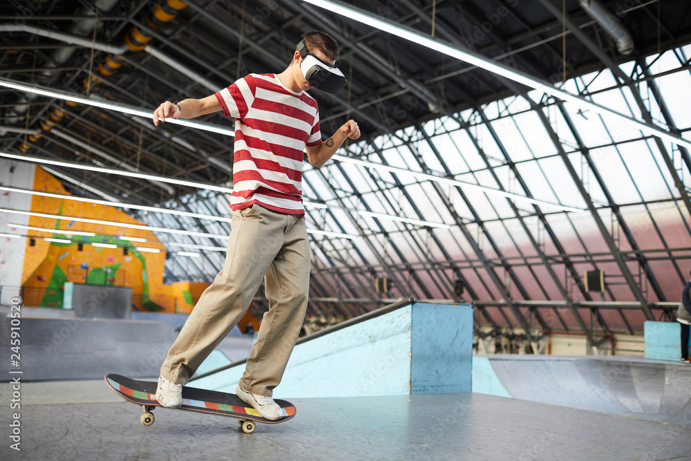 Young casual lad with vr headset standing on skateboard while moving along  flat surface of parkour area Stock Photo | Adobe Stock