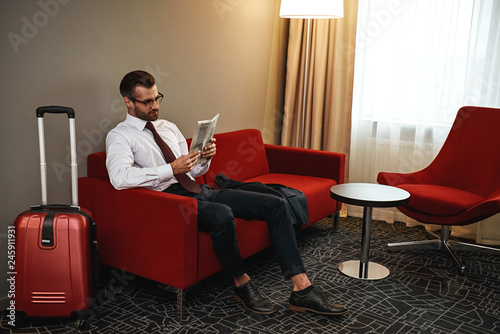 Spectacled business man with newspaper sitting on sofa at hotel hall
