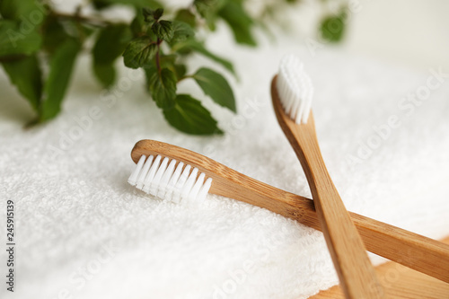 Fototapeta Naklejka Na Ścianę i Meble -  Close up of two bamboo toothbrushes on white towel with plant on background