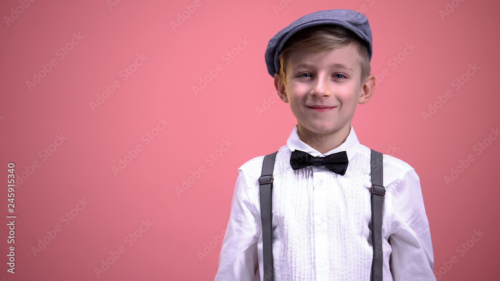 Funny little boy in vintage clothes smiling on camera against pink background - obrazy, fototapety, plakaty 