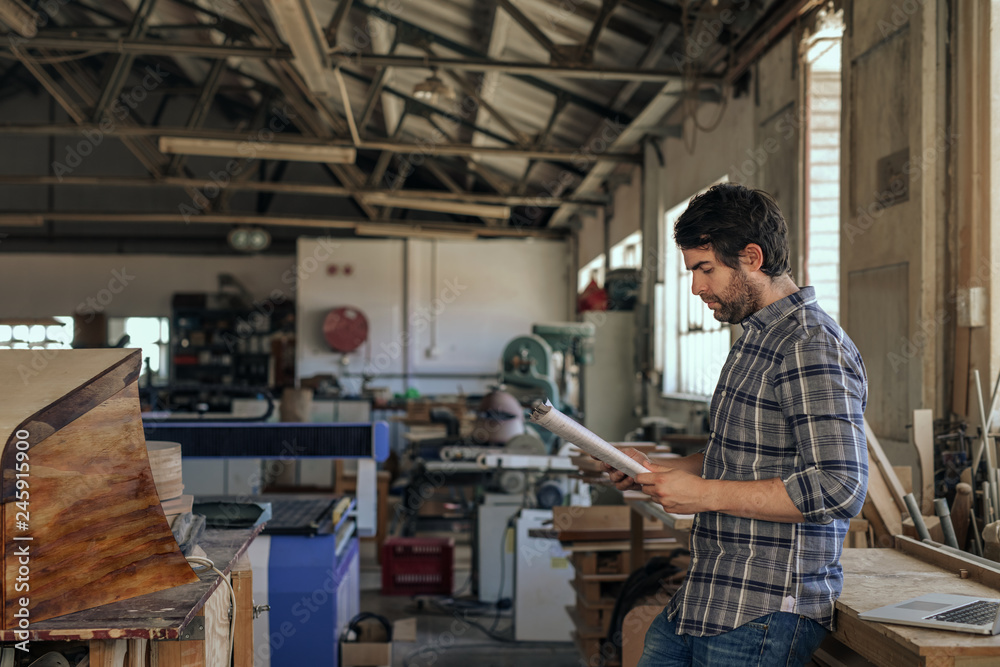 Woodworker reading through a design notebook in his workshop Woodworker reading through a design notebook in his workshop