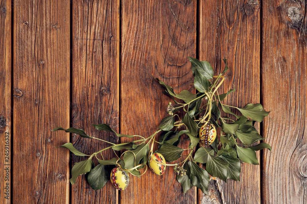 A top view of yellow hand painted easter eggs decorated with green ivy branches on a vintage, wooden table with space A top view of yellow hand painted easter eggs decorated with green ivy branches on a vintage, wooden table with space