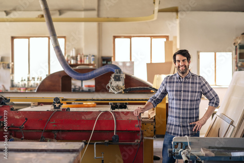 Smiling woodworker standing by equipment in his workshop