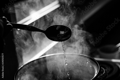 the man stirs the soup in the pan from which steam comes