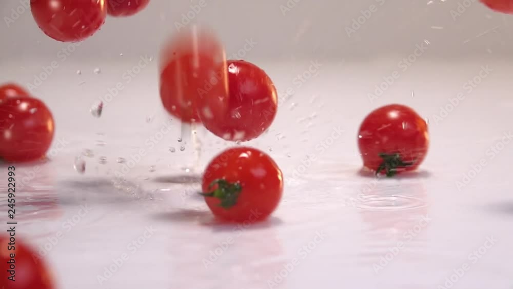 Red tiny tomatoes falling in water on white table in white wall background. Slow Motion 240 fps Red tiny tomatoes falling in water on white table in white wall background. Slow Motion 240 fps