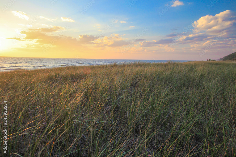 Dune Grass Sunset. Beautiful beach background with golden dune grass in the foreground and a vibrant sunset sky at the horizon on the coast of Lake Michigan.