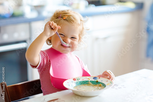 Adorable baby girl eating from spoon vegetable noodle soup. food, child, feeding and development concept. Cute toddler child, daughter with spoon sitting in highchair and learning to eat by itself photo