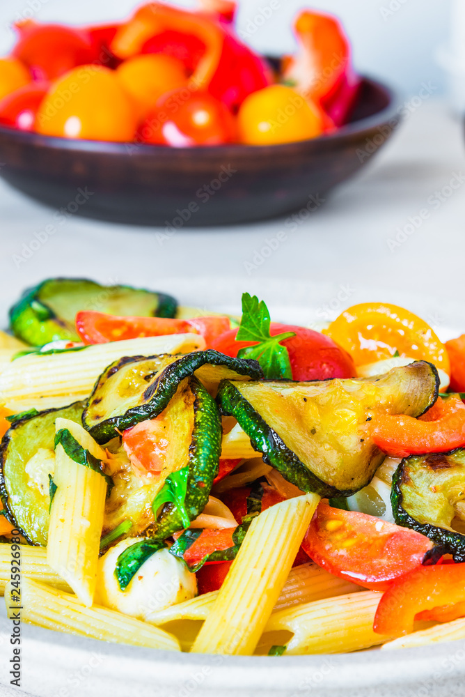 Margarita pasta on a plate and cherry tomatoes in the background - penne with tomatoes, zucchini, mozzarella and basil. Margarita pasta on a plate and cherry tomatoes in the background - penne with tomatoes, zucchini, mozzarella and basil.