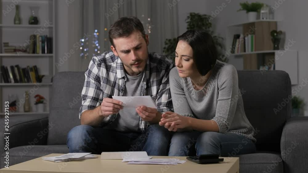 Amazed couple reading good news on a receipt sitting on a couch at home in the night Amazed couple reading good news on a receipt sitting on a couch at home in the night