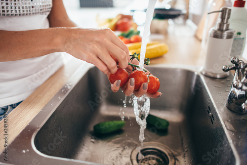 Woman washing tomatoes in kitchen sink close up.