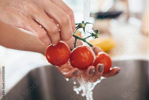Fotografie Woman washing tomatoes in kitchen sink close up.
