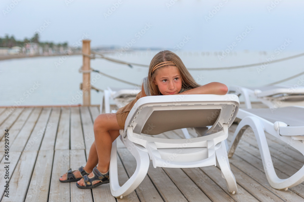 Portrait of pretty young gill  looking at camera enjoying sunny day on the sea beach lying on sun lounger