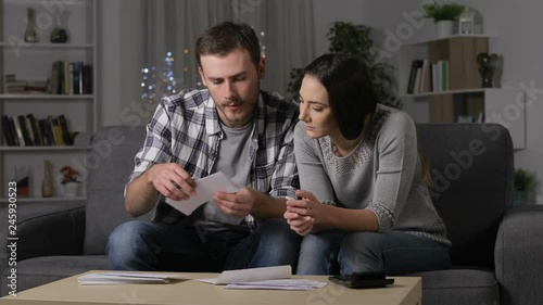 Excited couple receiving good news reading a receipt sitting on a couch at home in the night