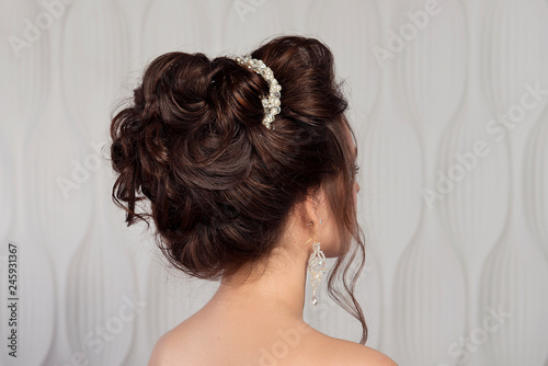 Wedding female hairstyle medium beam on the head of a brunette girl close-up rear view on a light background.