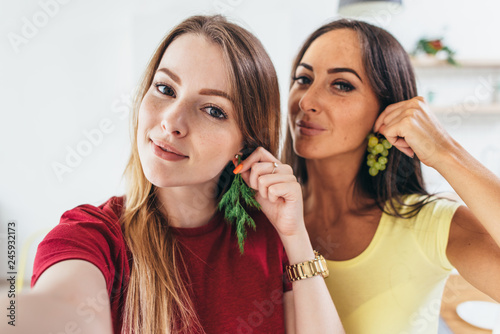 Female friends taking selfie whilst making breakfast in kitchen.