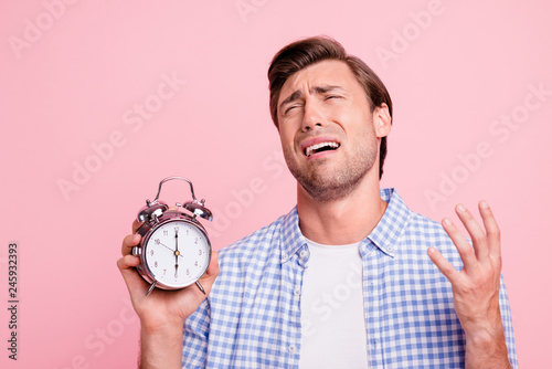 Close up photo of beautiful amazing brunet he him his handsome with metal alarm clock in hand arm complaining hate working early wearing casual checkered plaid shirt outfit isolated on rose background