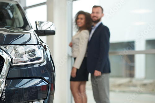 Couple posing behind automobile in car canter.