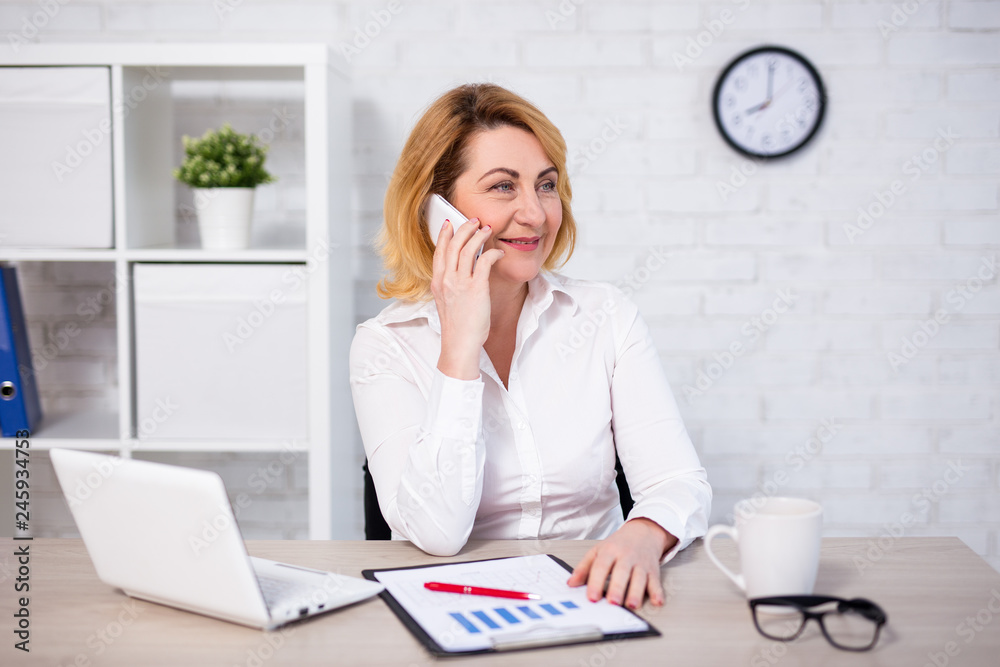 happy mature business woman sitting in office and talking by phone happy mature business woman sitting in office and talking by phone